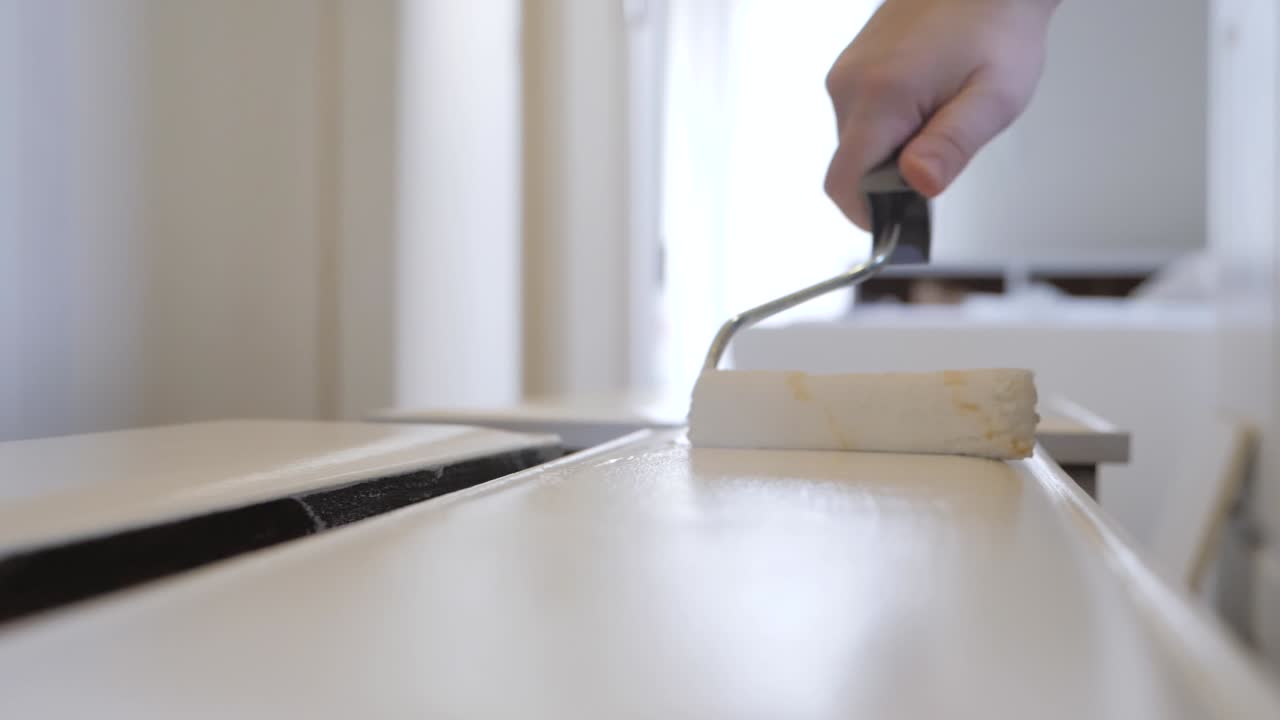 pintura blanca siendo pintada en un cajón usando un rodillo de pintura para renovar una pieza antigua de muebles