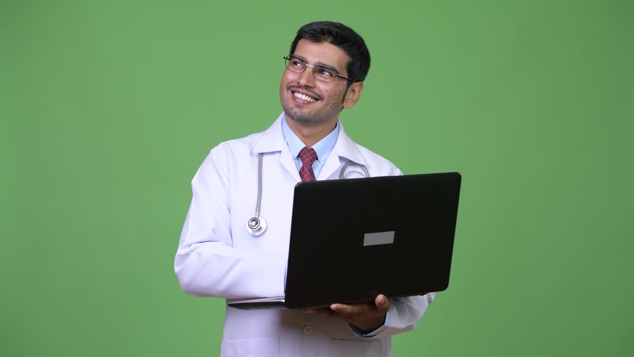 Young handsome Persian man doctor using laptop