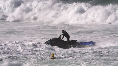 Die-Kamera-Jagt-Einen-Jetski-Fahrer,-Der-Gegen-Die-Wellen-Kämpft,-Und-Einen-Surfer,-Der-Den-Schäumenden-Wellen-Nicht-Entkommen-Kann