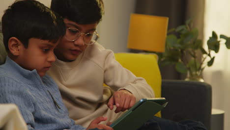 two young boys sitting on sofa at home playing games or streaming onto digital tablet together 2