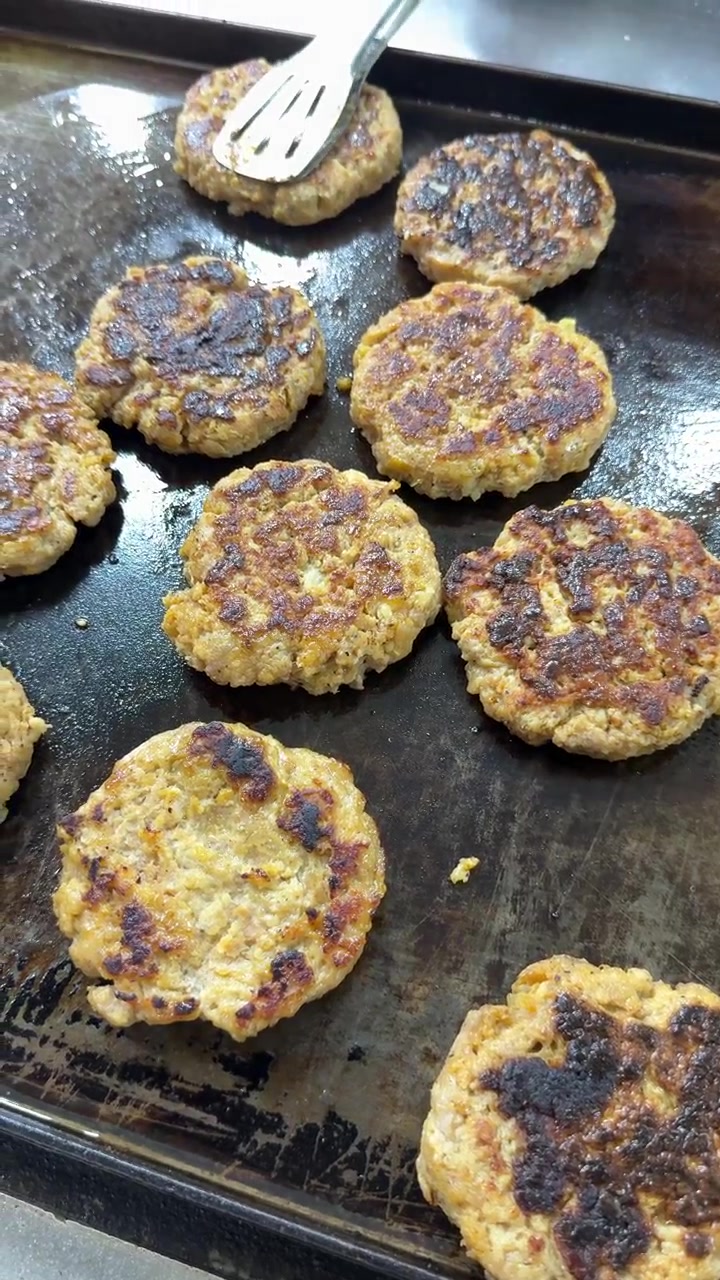 Chef Using Tongs to Flip Burger Patties on a Hot Griddle