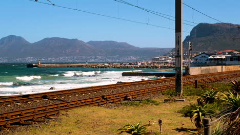 view of kalk bay harbour from over old railway tracks, waves breaking on shore