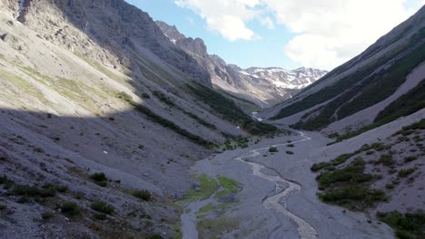 aerial drone footage flying through a dramatic glacial valley surrounded by a steep mountains and pine trees with patches of snow and an alpine river in switzerland