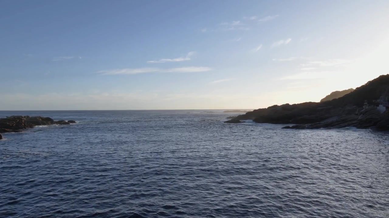 Bewegte Aufnahme über die Hängebrücke am Storms River Mouth, Tsitsikamma-Nationalpark, Südafrika, wo Ozeanwasser auf eine zerklüftete Felsküste trifft und die ruhige Schönheit in der Dämmerung zeigt.