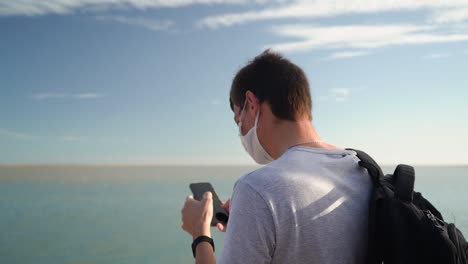 Turista-Mochilero-Usando-Un-Smartphone-En-El-Soleado-Puerto-Marítimo-De-Puerto-Ingeniero-Blanco,-Buenos-Aires,-Argentina