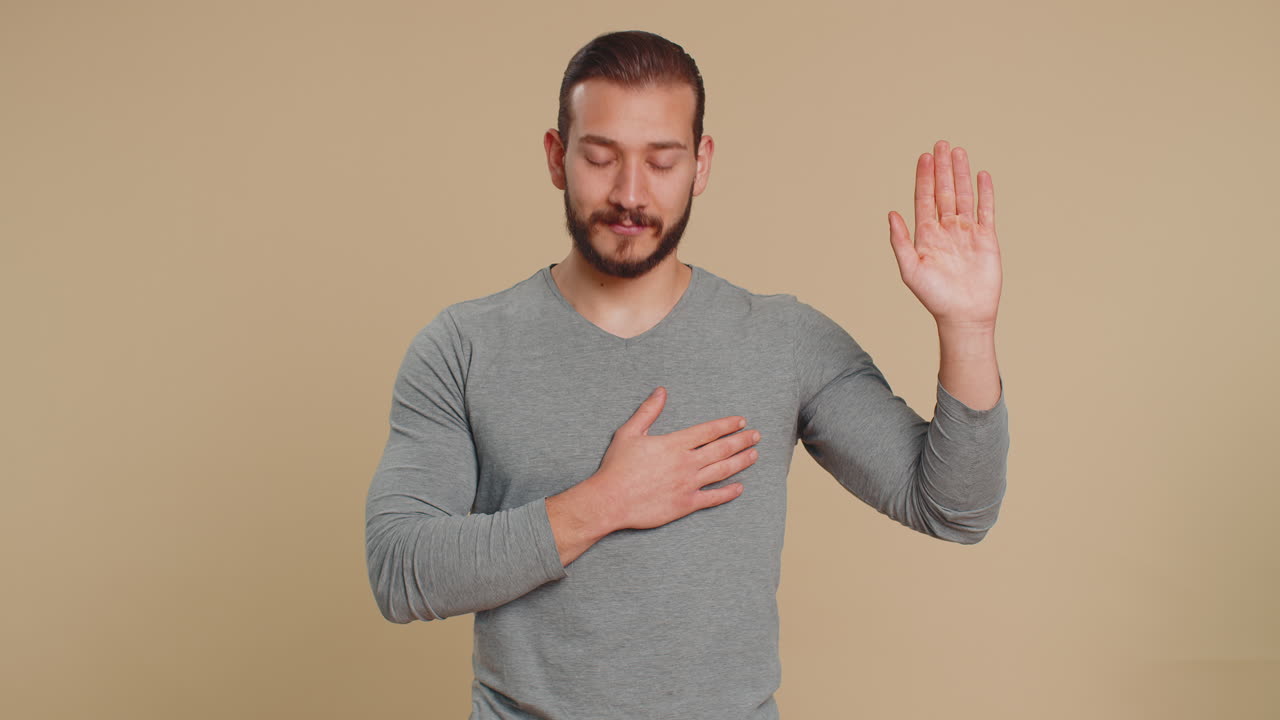 Young man raising hand to take oath promising to be honest and to tell truth keeping hand on chest