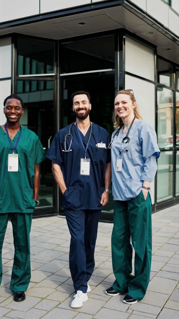 Fotogramma di un video di tre operatori sanitari sorridenti in camice, ripresi da un angolo basso all'esterno