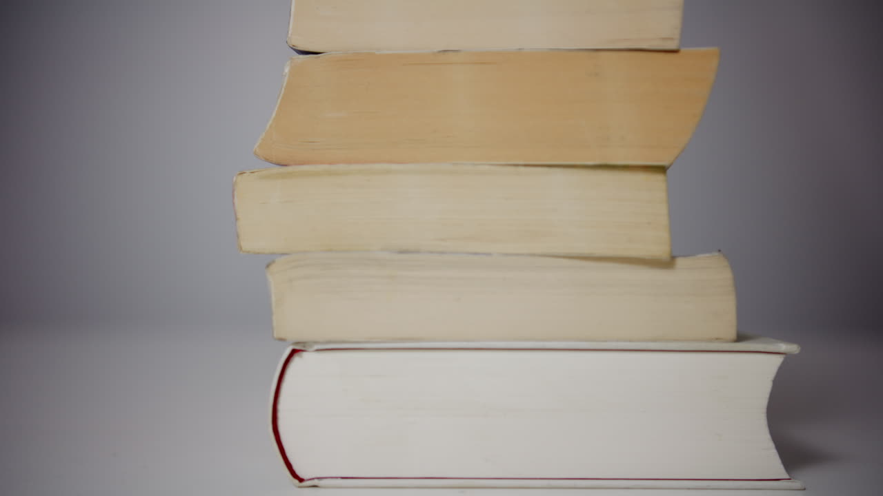 Side view of a stacked pile of books filmed with a slow left to right camera movement, creating a calm and timeless concept of knowledge, education, and experience
