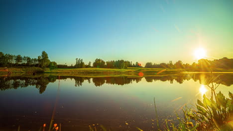 Timelapse-shot-of-sun-setting-over-green-grasslands-along-the-sides-of-a-lake-during-evening-time