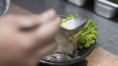 close-up shot of a hand preparing fresh ceviche with lime, onion, and lettuce