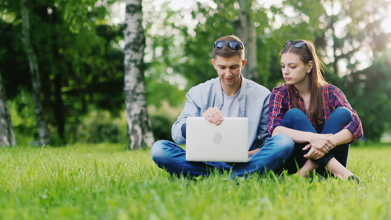 comenzó con una computadora portátil en el parque el hombre abre la computadora portátil sentada al lado de una mujer video hd