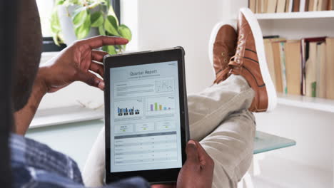african american man relaxing at home, reviewing quarterly report on tablet
