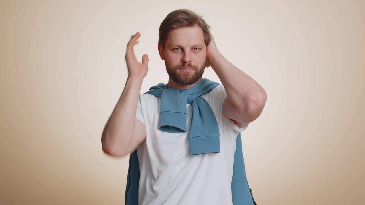 짜증나서 짜증나서 잘생긴 남자가 귀를 가리고 몸짓을 하고 조언을 피하지 않고 소음을 무시하고 큰 목소리를 내고