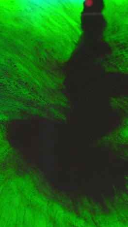 vertical video of black and green paint or dye dropped into water against white background to create swirling colourful smoke background