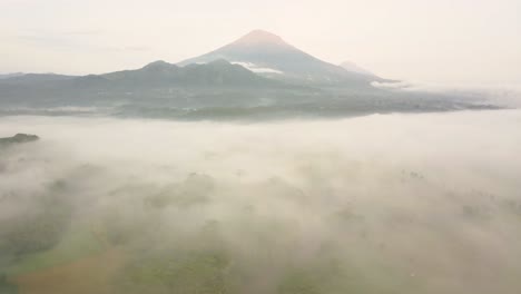 cinematic drone panoramic of beautiful indonesian scenery with hovering clouds and mist during sunny day - silhouette of mount sumbing in background - sun flares lighting during daytime