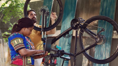 mujer negra arreglando bicicleta con computadora portátil