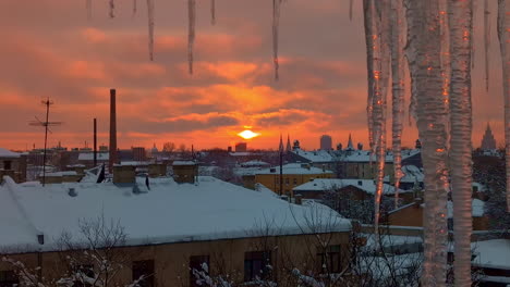 red sunset sky and snowy city rooftops with icicle in foreground