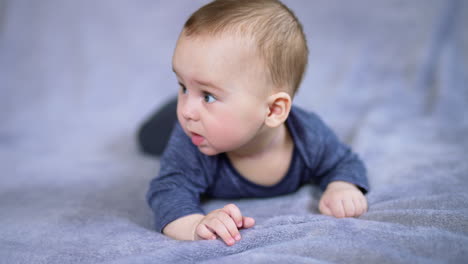 caucasian boy in blue shirt resting on big grey plaid. adorable baby moves his feet and turns his head. grey backdrop in blur.