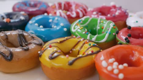 una gran cantidad de rosquillas con esmaltes de frutas en diferentes colores se muestran en la mesa blanca. vertido con chocolate blanco y oscuro con salpicaduras de pastelería. dulces de primer plano. concepto de obesidad