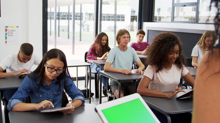 Teacher uses tablet in high school class, over shoulder view