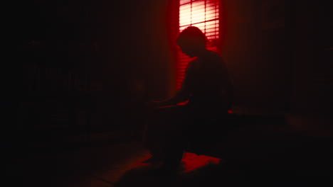 woman sits on sofa as red light silhouettes her from window