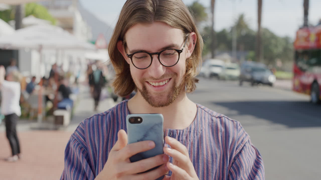 ritratto di un giovane felice che usa uno smartphone, si diverte a navigare online, a mandare sms, a condividere le vacanze sui social media, sullo sfondo di una vivace spiaggia urbana, comunicazione digitale