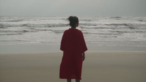 chica con una camisa naranja mirando hacia las olas del mar en una playa en un día nublado en la india - chica disfrutando de una mañana en la playa