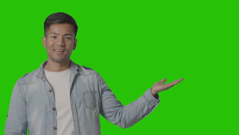 studio shot of casually dressed young man presenting or showing against green screen