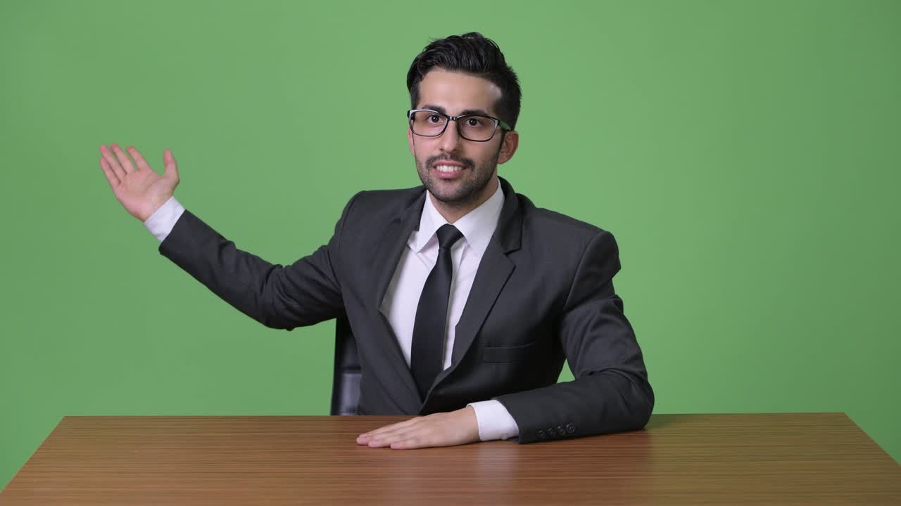 Young handsome bearded Persian businessman against green background