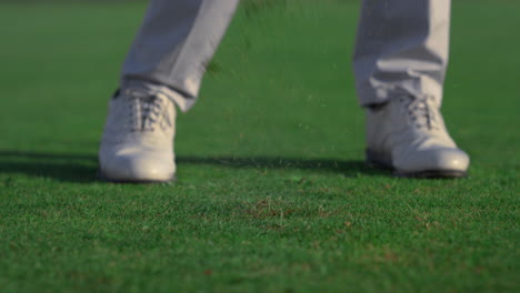 man legs swinging golf putter club on course field. player feet stand on grass.