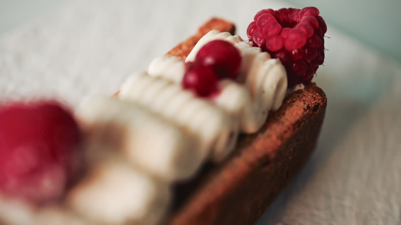 Close up of a gourmet pastry topped with cream, raspberries, and red currants