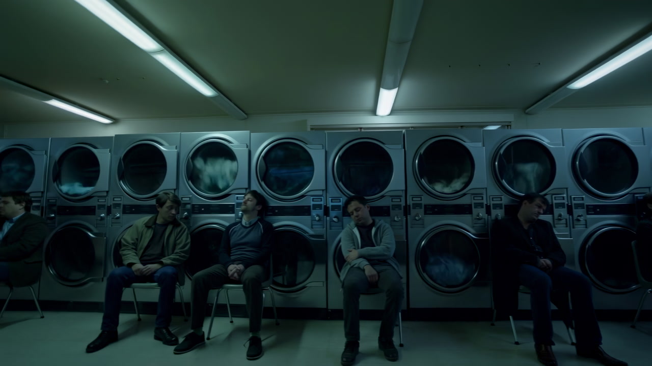 Moody Laundromat Night Seated Customers Waiting On Metal Chairs Under Fluorescent Lights Rows Of Frontload