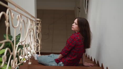 mujer joven sentada en las escaleras en una camisa a cuadros roja y vaqueros