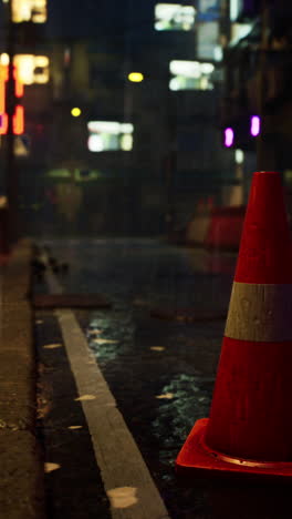 un cono de tráfico se sienta en una calle húmeda en una ciudad por la noche