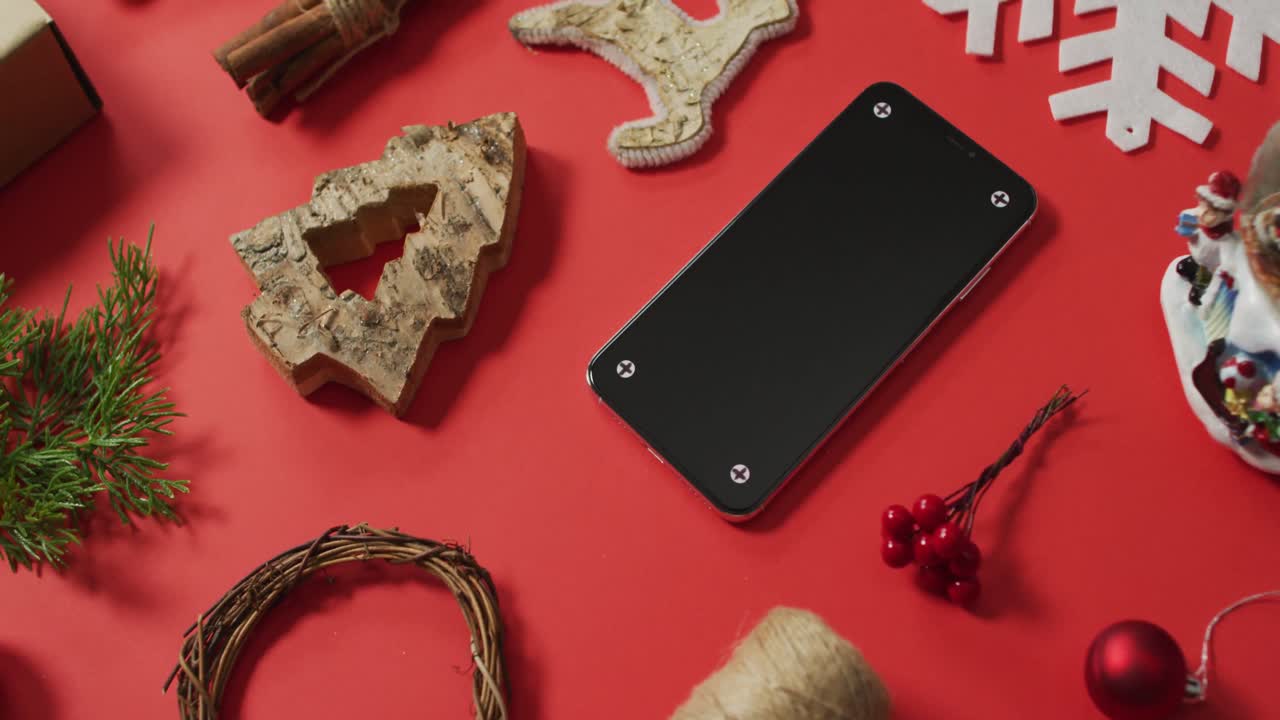 video de decoraciones de navidad y rama de árbol con teléfono inteligente sobre fondo rojo