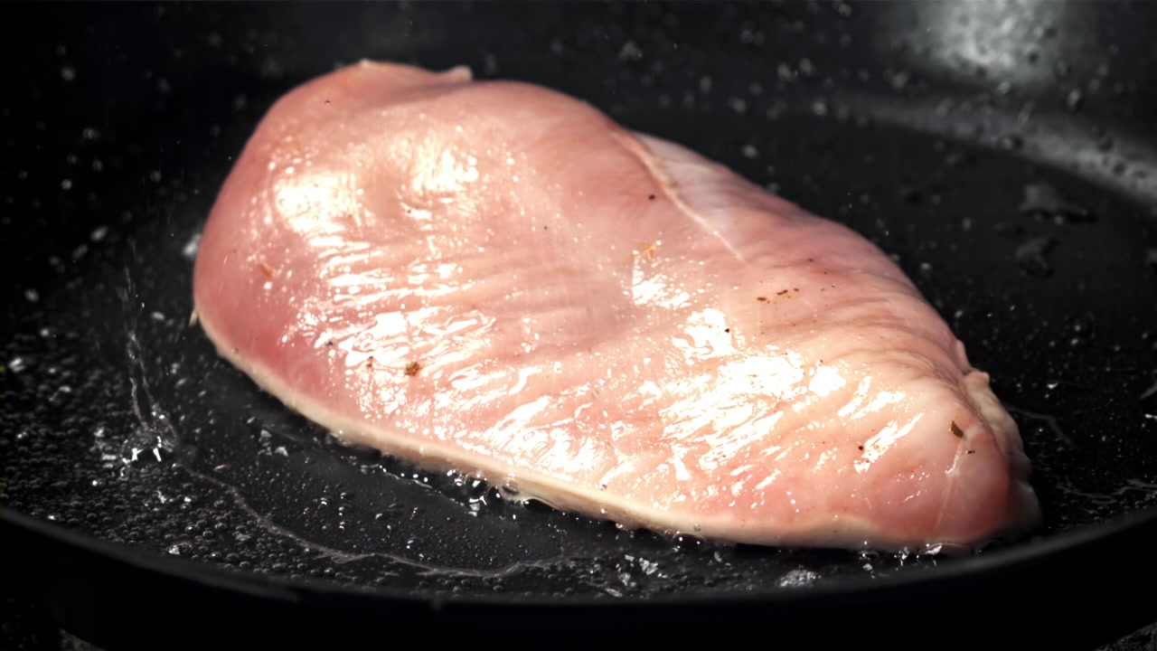 Pollo crudo friéndose en una sartén caliente con aceite chispeante