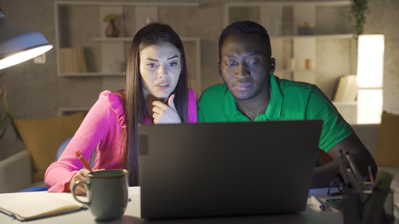 African young man and Caucasian young woman working in home office discussing work using laptop.