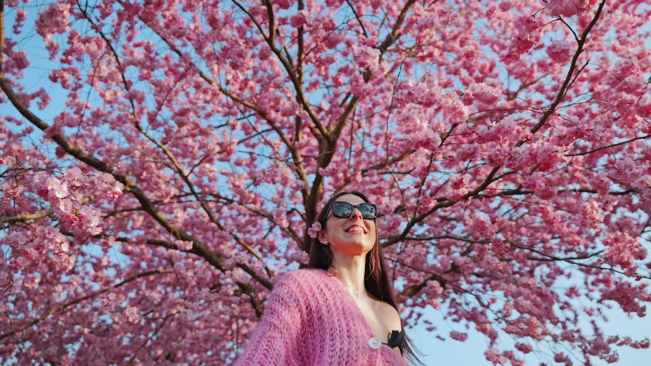 Vibrant spring energy, slow motion as woman leaps happily under cherry tree