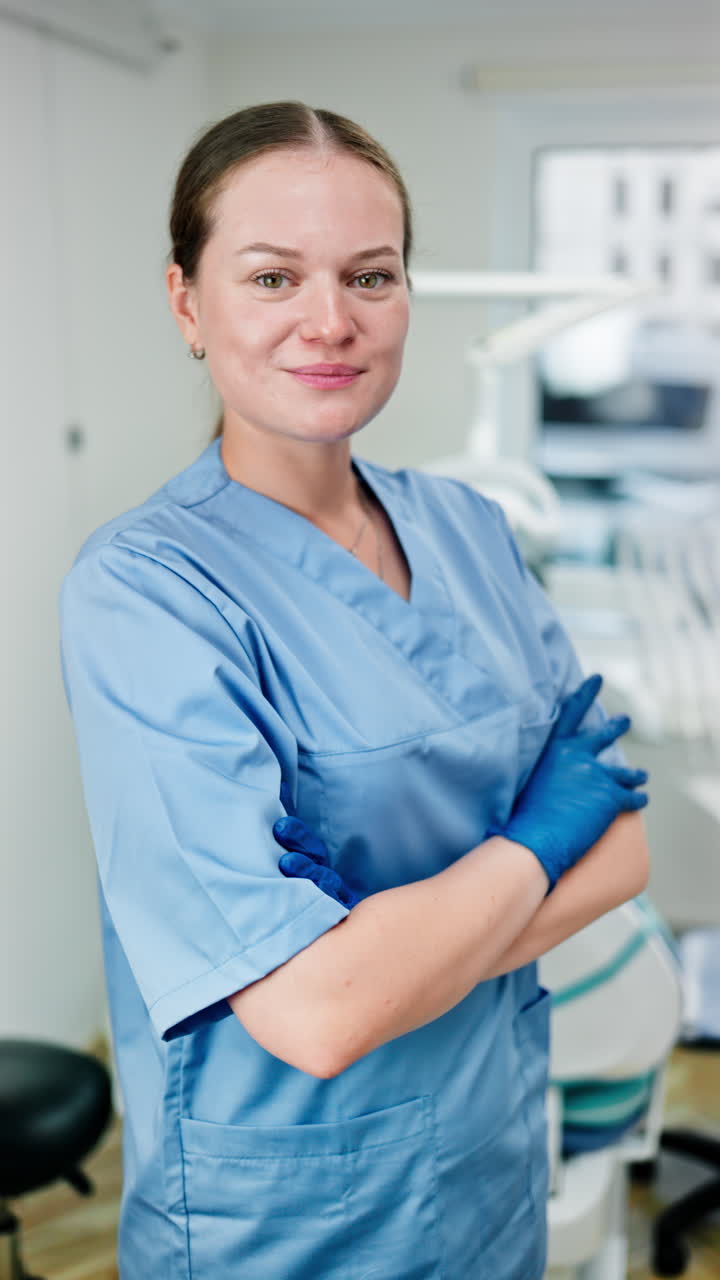 Dentist wearing a scrub and standing and smiling in a dental cabinet. Vertical