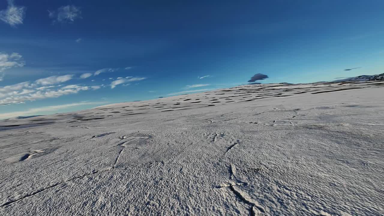 The FPV drone returns over the frozen lake, skimming inches above the ice and snapping into a mid-air direction change, carving across cracked textures on Lake Heiðarvatn’s winter surface