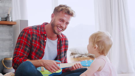 Young-dad-playing-ukulele-with-toddler-daughter,-close-up