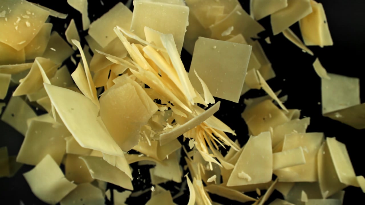 Copeaux de parmesan tombant au ralenti sur fond noir.