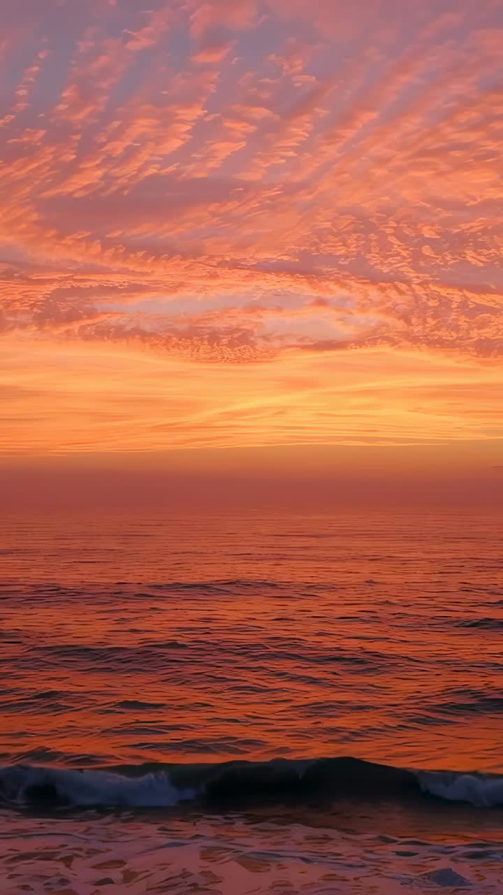 Vertical video: Shifting sunset light causing rolling ocean at shore, with rippled cloud bands