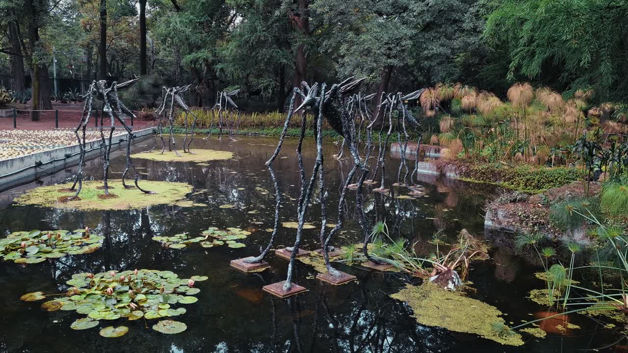 Artistic metal sculptures rise from a pond surrounded by lush vegetation in Chapultepec Park, Mexico City