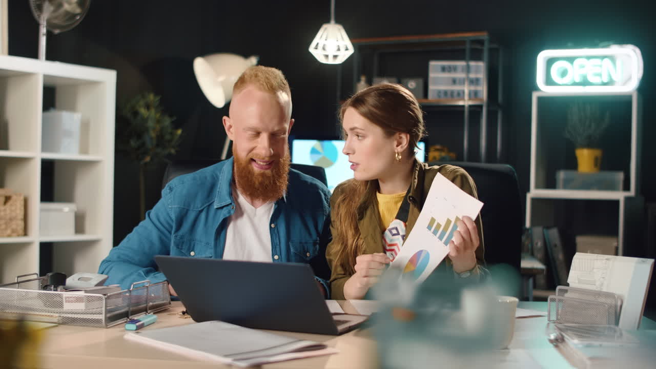 Young business couple showing documents in front of laptop screen in office