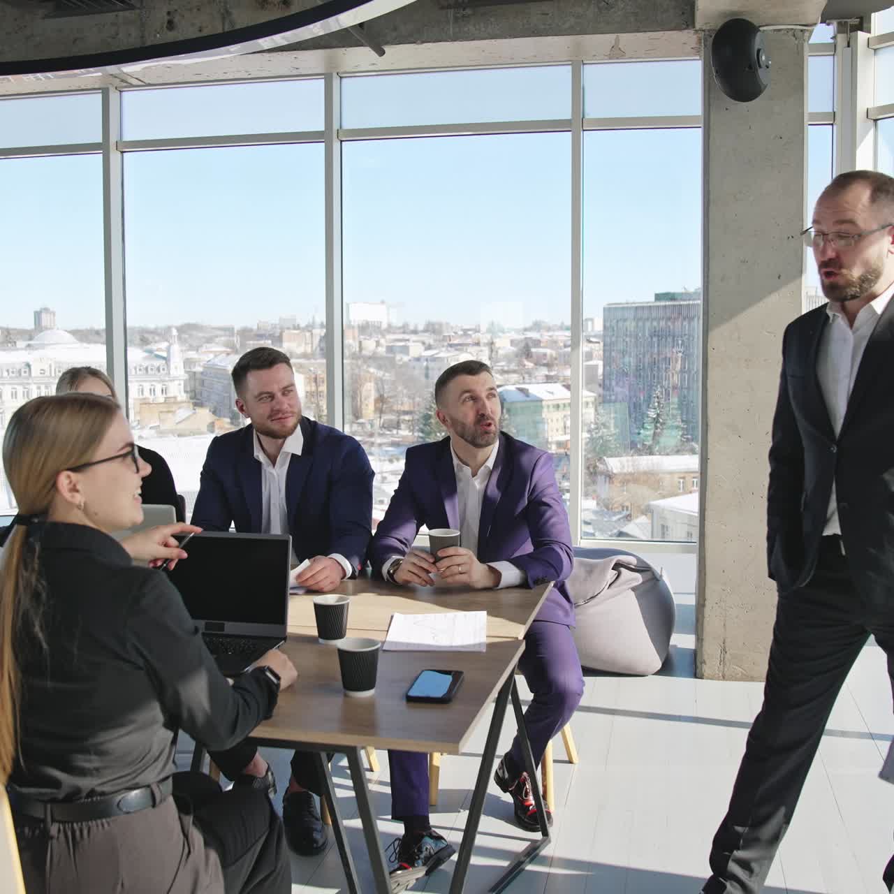 Teammates discussing strategies sitting at the table. Colleagues have a meeting in a sunny office space. Cityscape at the backdrop