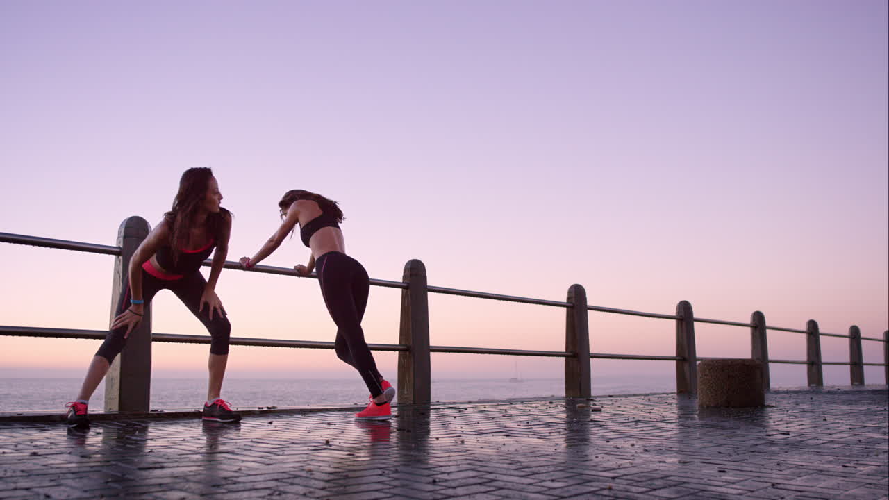 dos amigos atléticos estirándose después de una carrera en el paseo marítimo al atardecer