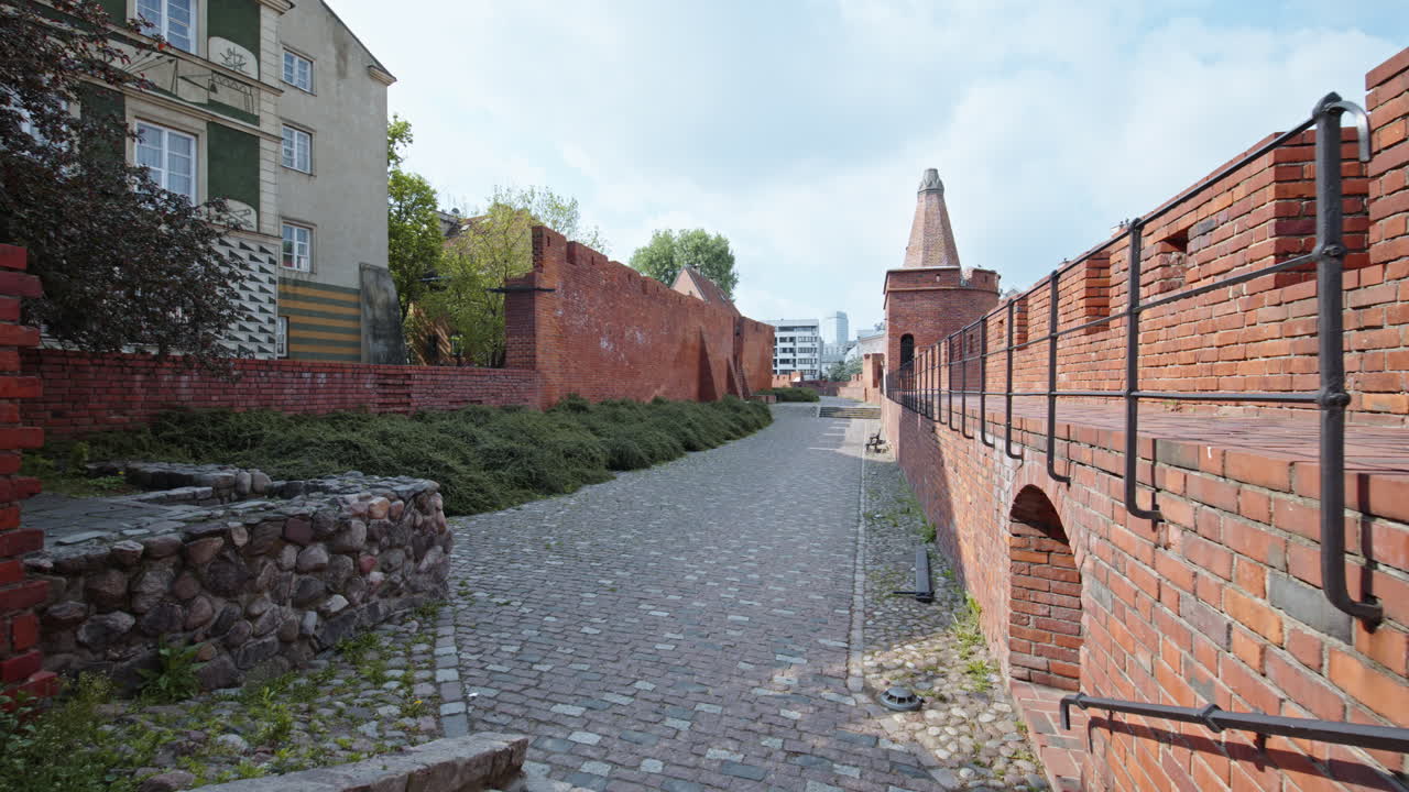 Cobblestone path near the Barbakan fortress, Warsaw, showcasing brick walls and greenery