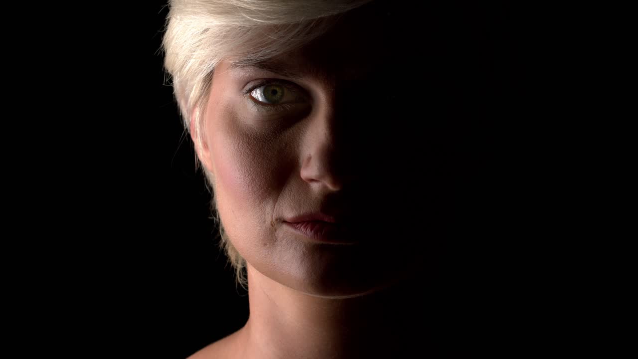 A serious woman looks straight into the camera, half face shaded. Depression, menthal problem or abuse concept