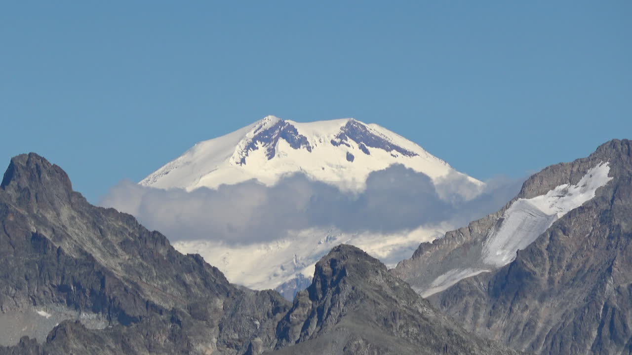 Riprese panoramiche di una cima montuosa innevata che si erge sopra creste rocciose e nuvole vicino a Dombay, Caucaso, Russia, ideali per temi di viaggio, natura e avventura.